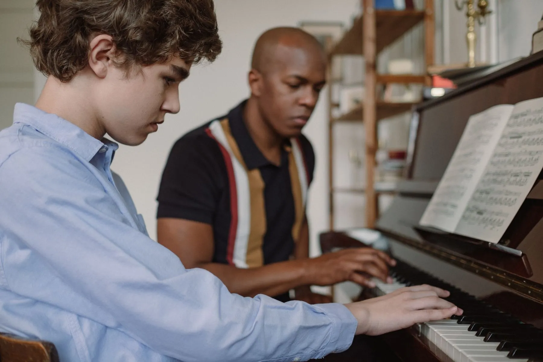 Professor de piano acompanhando um aluno adolescente